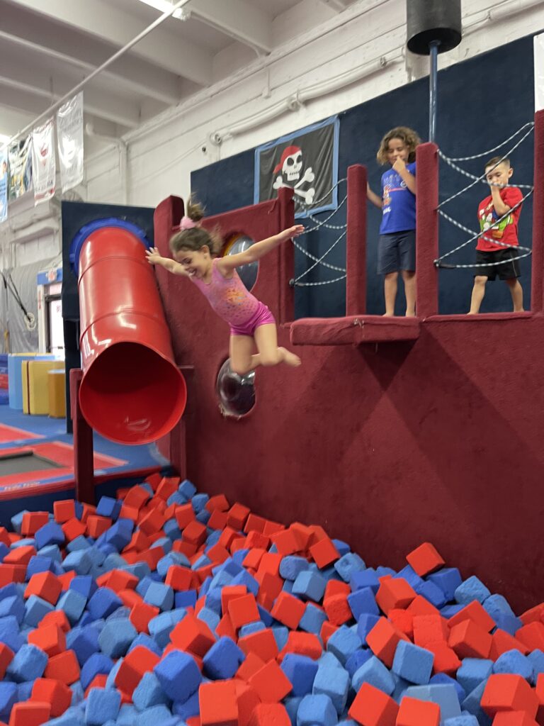 Gymnastics Camps American Twisters gymnast in red leotard on beam with arms up straight
